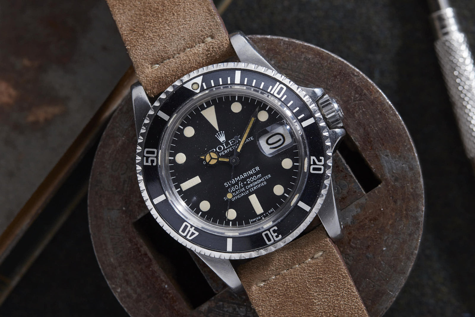 A Rolex Submariner dive watch by Rolex, featuring a brown leather strap, black dial with white markers, and date display, rests on a round metal object.