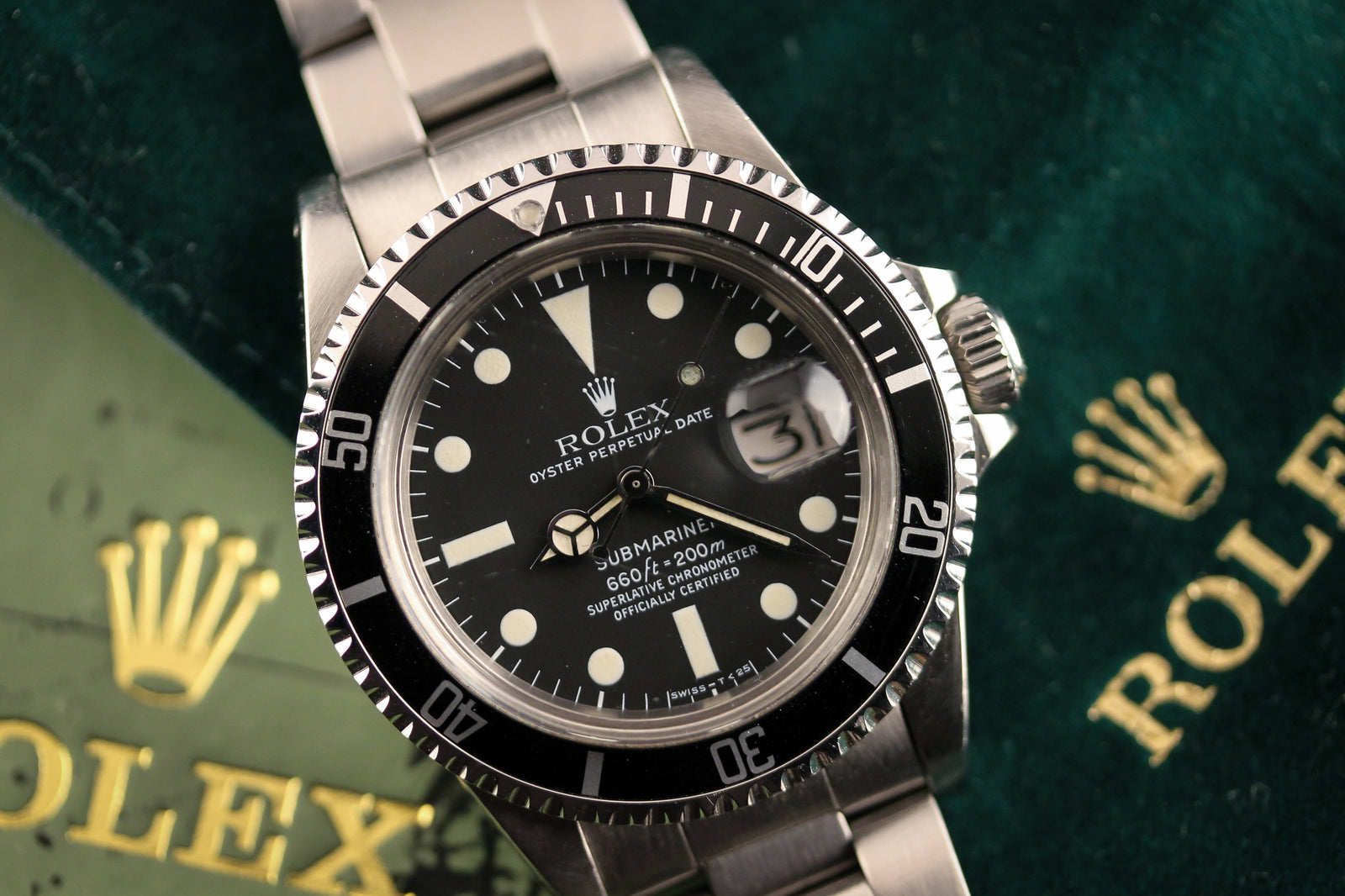 A close-up of the Rolex Submariner 1680 -1979 with stainless steel band, black dial, and white markers, resting on a green surface featuring the gold Rolex crown and text—a must-have for vintage Rolex enthusiasts.