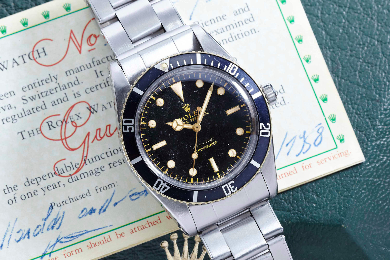 A Rolex Submariner 5508 dive watch with a black dial and silver band is displayed atop its original warranty certificate, which features handwritten notes and green text.