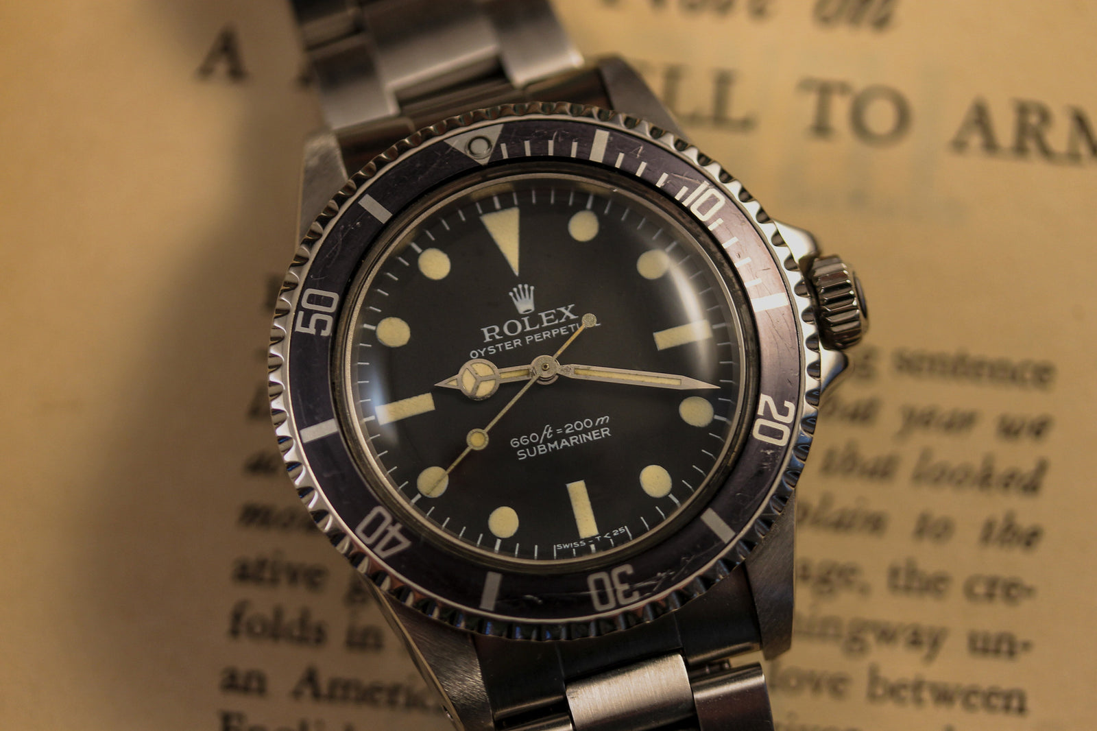 A close-up of the 1978 Rolex Submariner 5513 with a black bezel and dial, displaying 3:54, rests on an open book with blurred text in the background.
