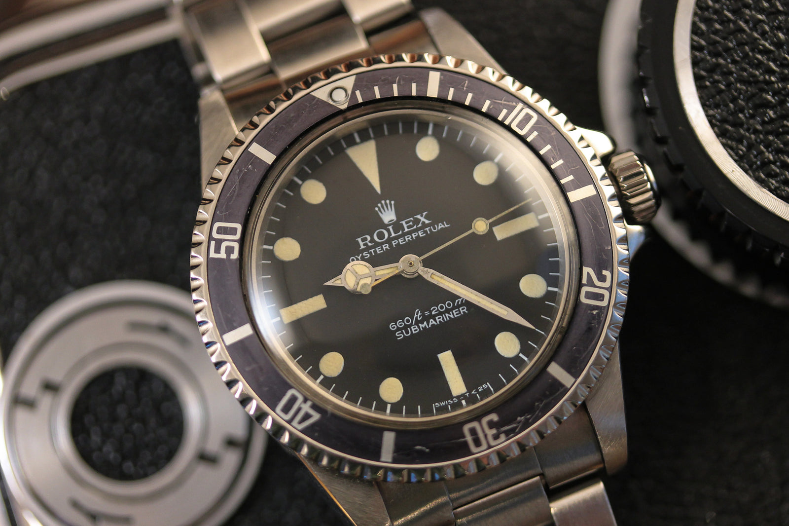 Close-up of a Rolex Submariner 5513 - 1978 by Rolex featuring a black dial, luminous hands and markers, stainless steel bezel and bracelet, displayed beside a camera lens on a dark surface.