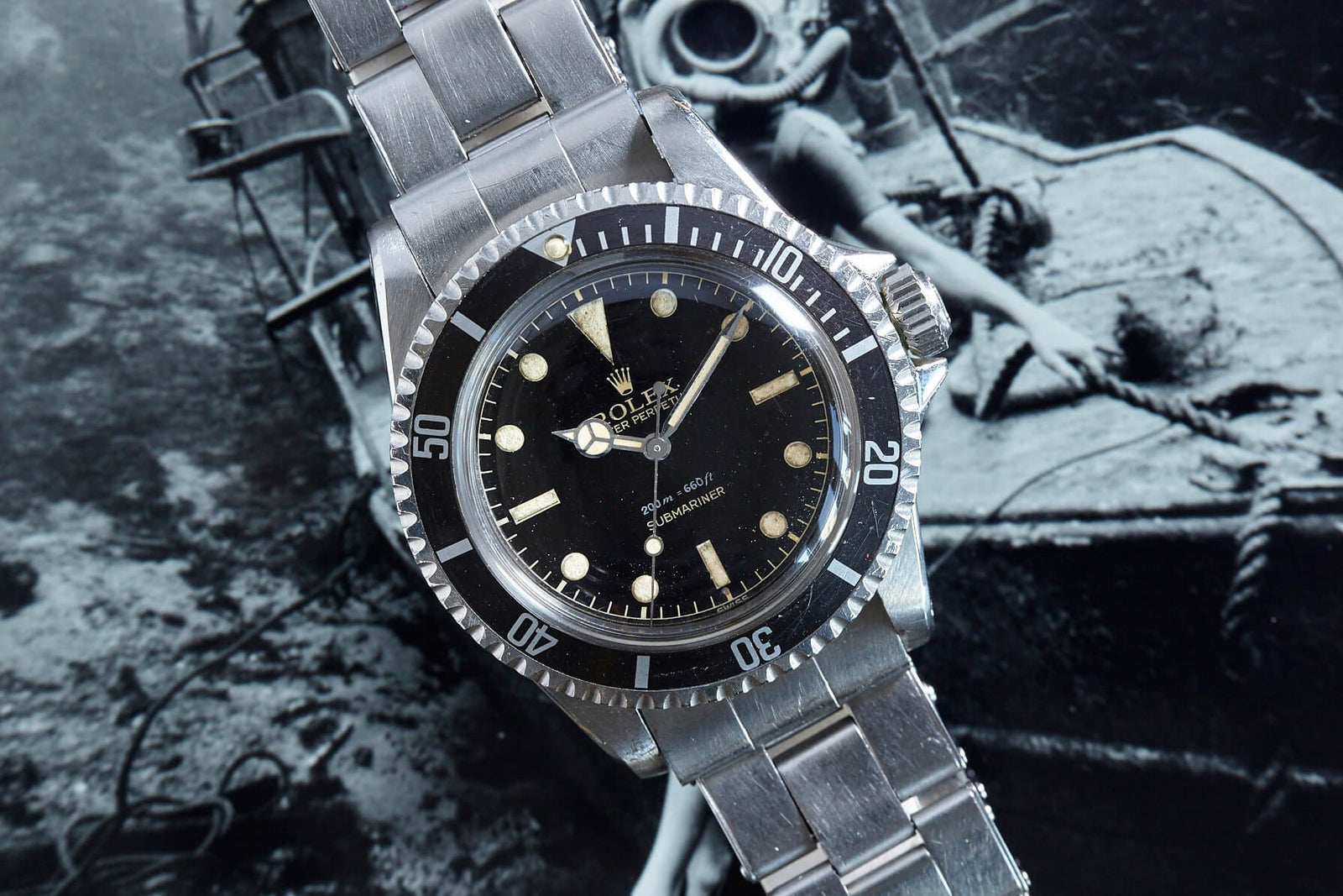 The Rolex Submariner 5513 Gilt Dial by Rolex, featuring a black dial and stainless steel bracelet, is showcased against a nautical-themed black-and-white backdrop.