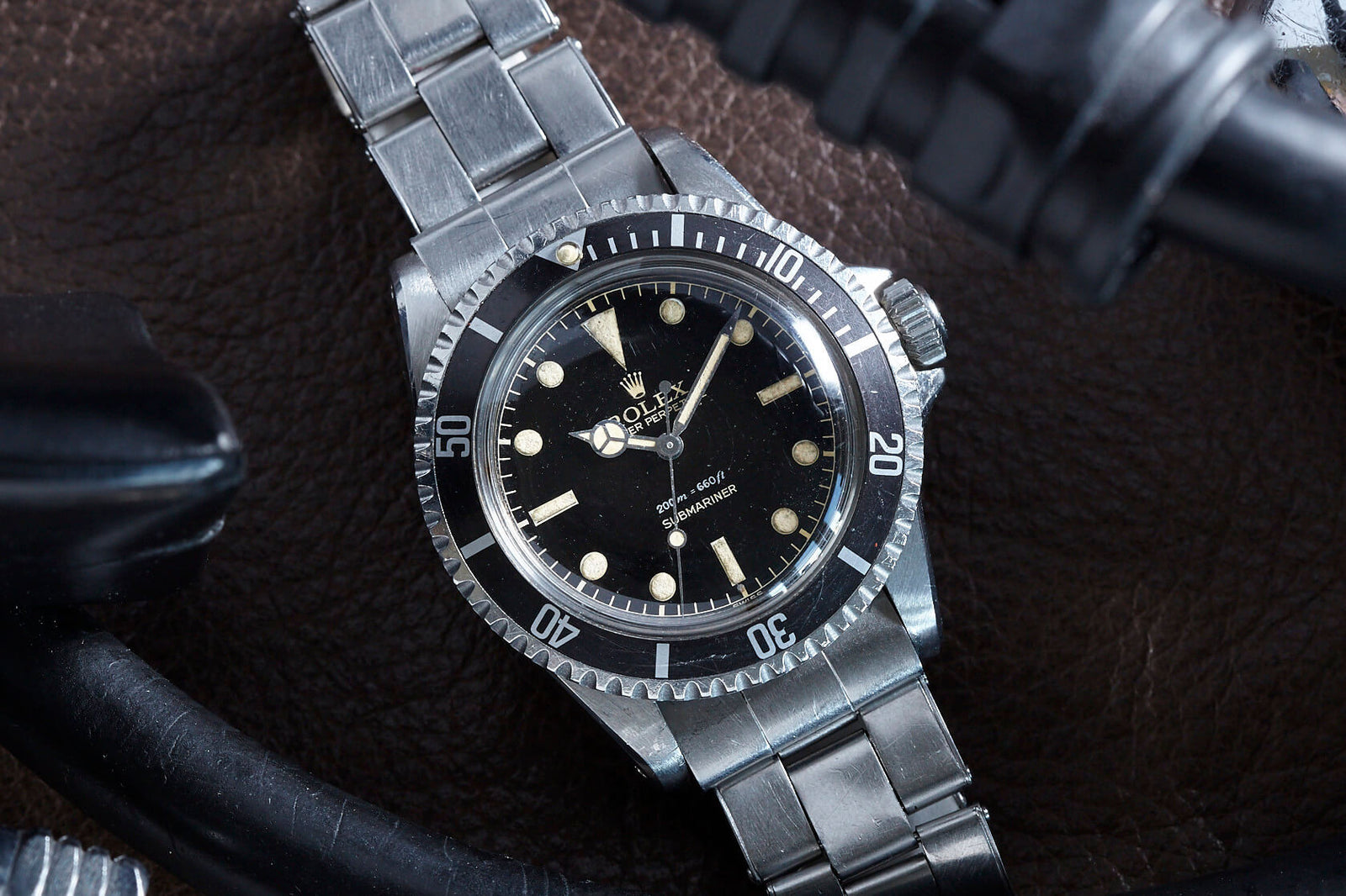 A close-up of the Rolex Submariner 5513 Gilt Dial, featuring a black dial and silver band, resting on a brown textured surface beside black diving equipment.