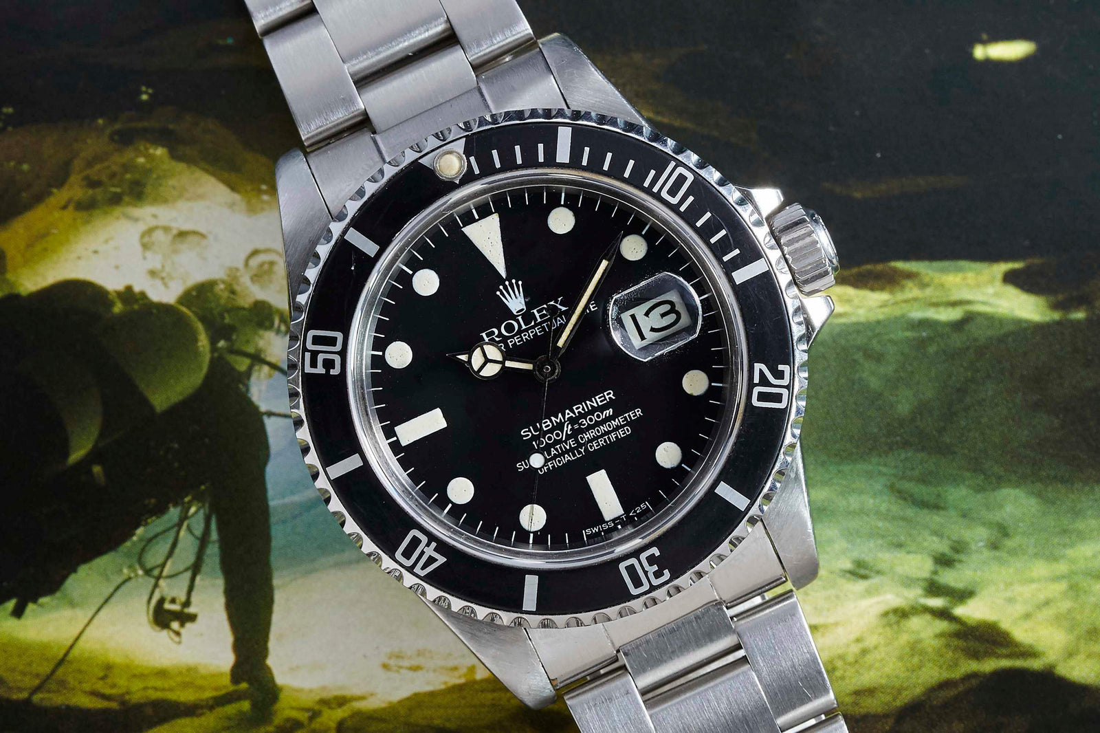 A close-up of the Rolex Submariner Date by Rolex, featuring a black dial and bezel, silver markers, stainless steel band, and date display set against an underwater diving backdrop.