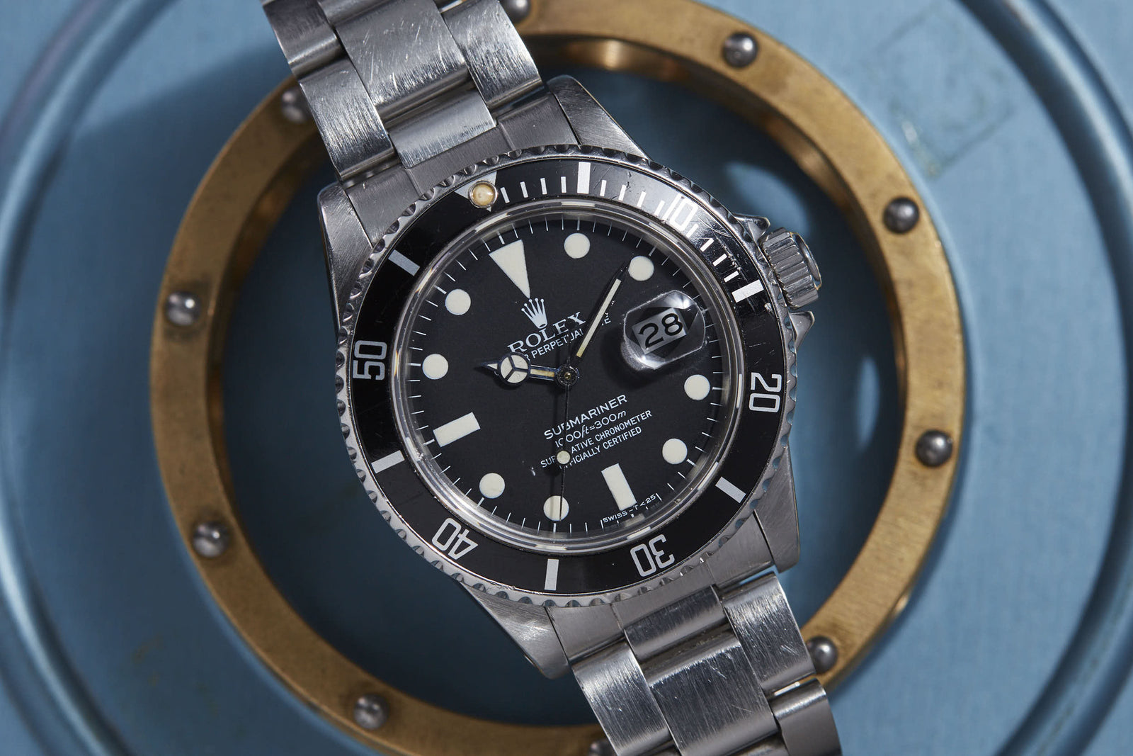 A Rolex Submariner by Rolex with a black bezel and dial is shown on a round metallic blue and brass background, displaying the time as 9:14 and the date as 23.