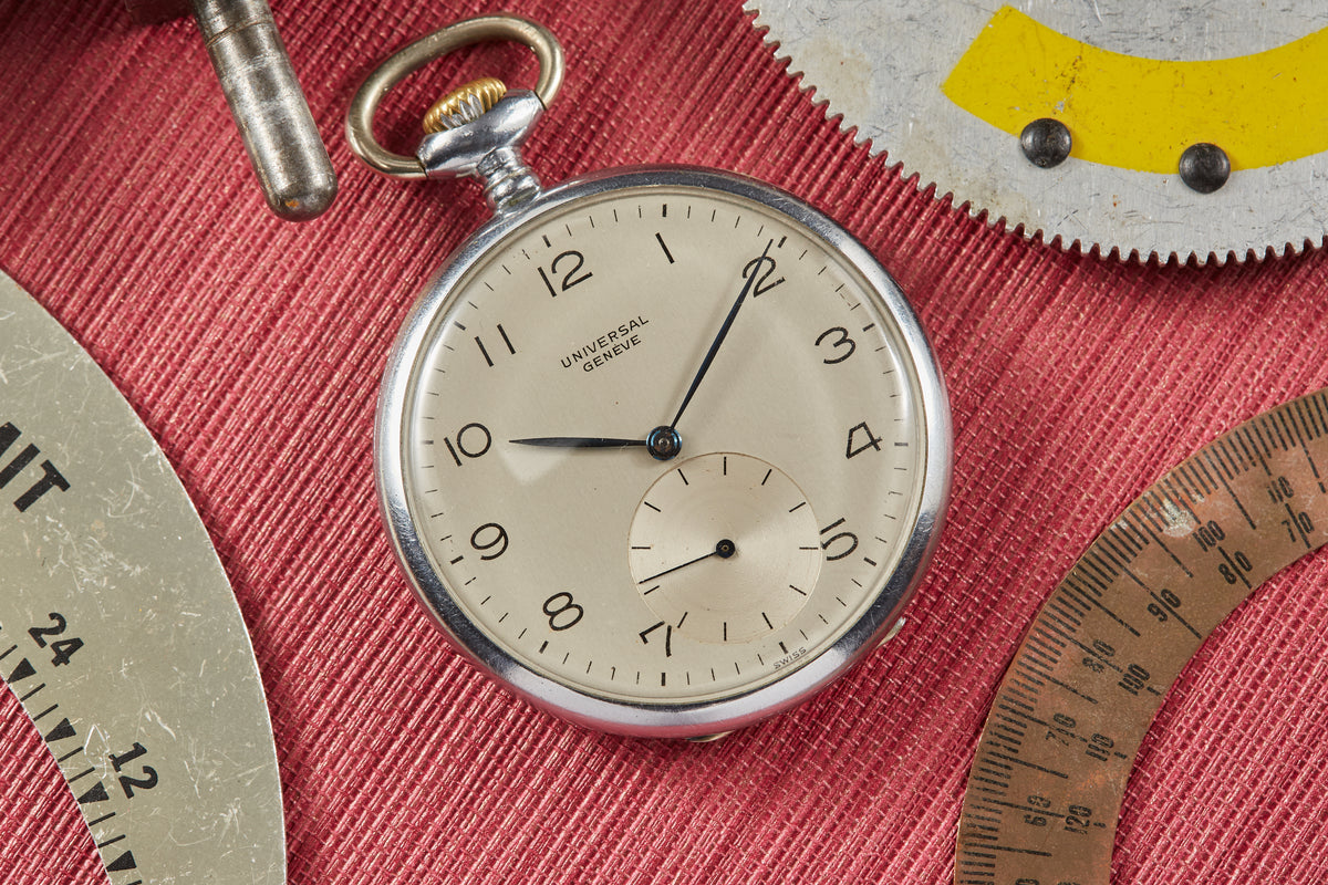Universal Genève pocket watch with cream dial, Arabic numerals, subsidiary seconds dial, and metal chain on burgundy fabric b