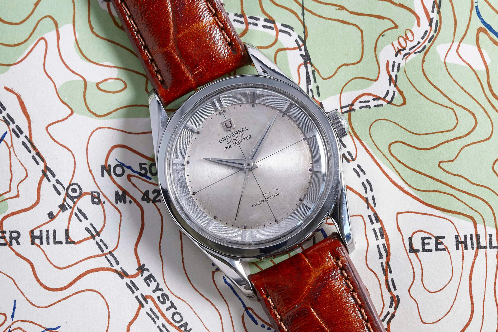 A Universal Geneve Polerouter with a brown leather strap rests on a colorful topographic map, which features contour lines and labeled locations such as Keystone Hill and Lee Hill.