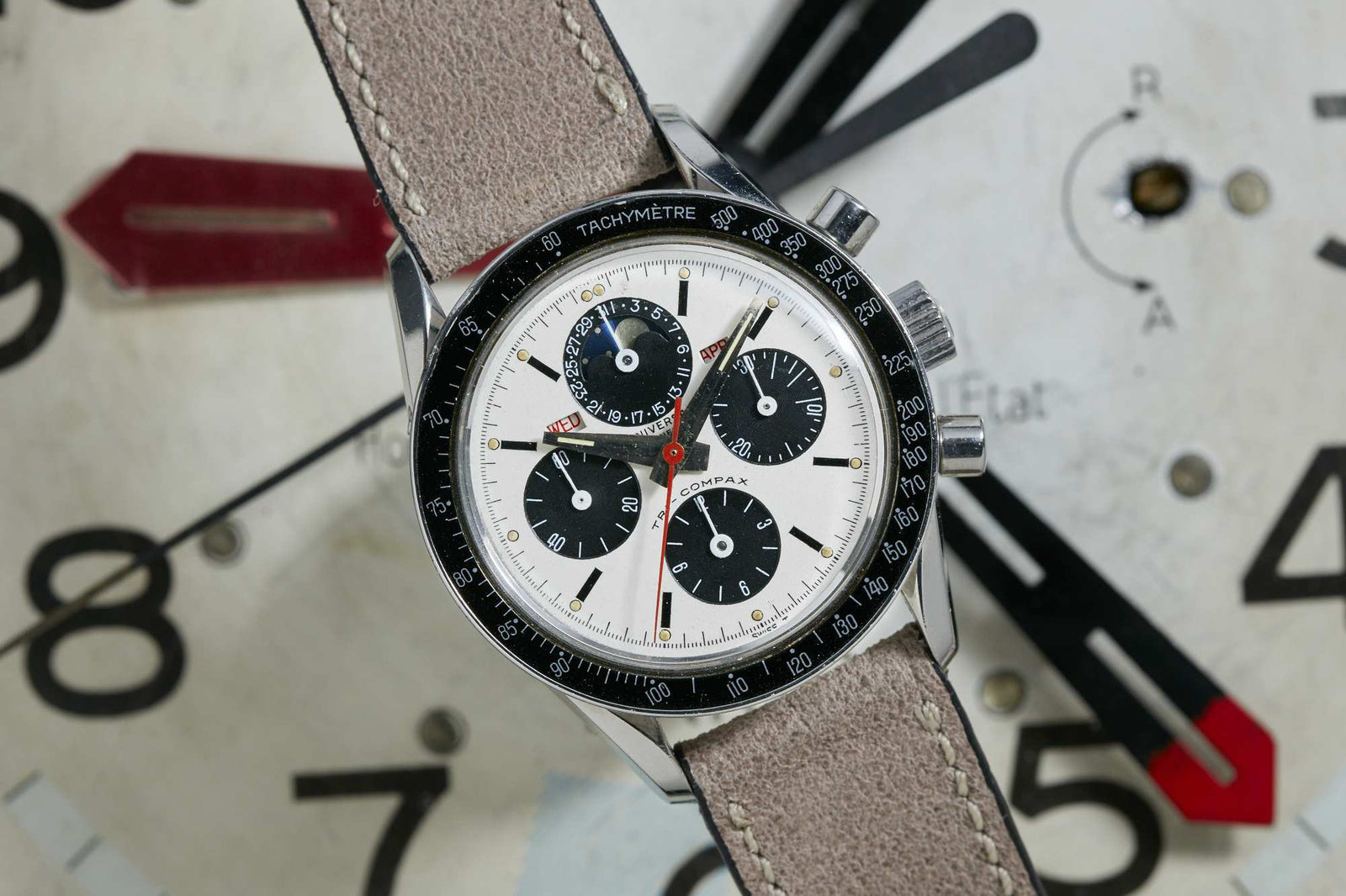 A close-up shows the Universal Geneve Tri-Compax chronograph with a beige strap, black tachymeter bezel, white dial, and three black subdials set against a large clock face with bold black and red hands and numbers.